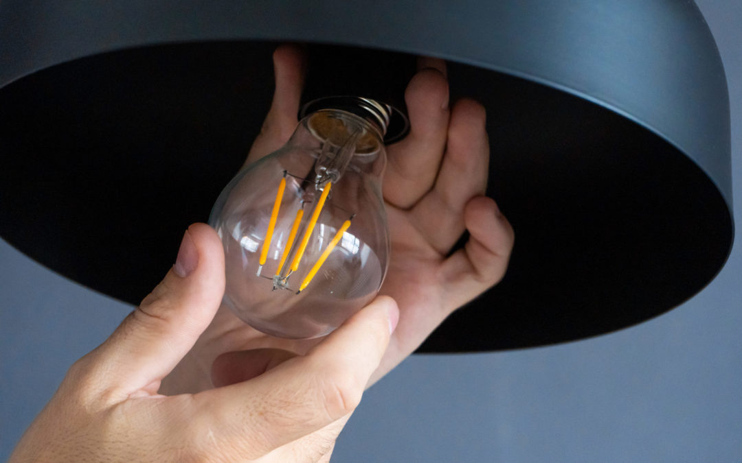 Close-up. A hand changes a light bulb in a stylish loft lamp. Spiral filament lamp. Modern interior decor.
